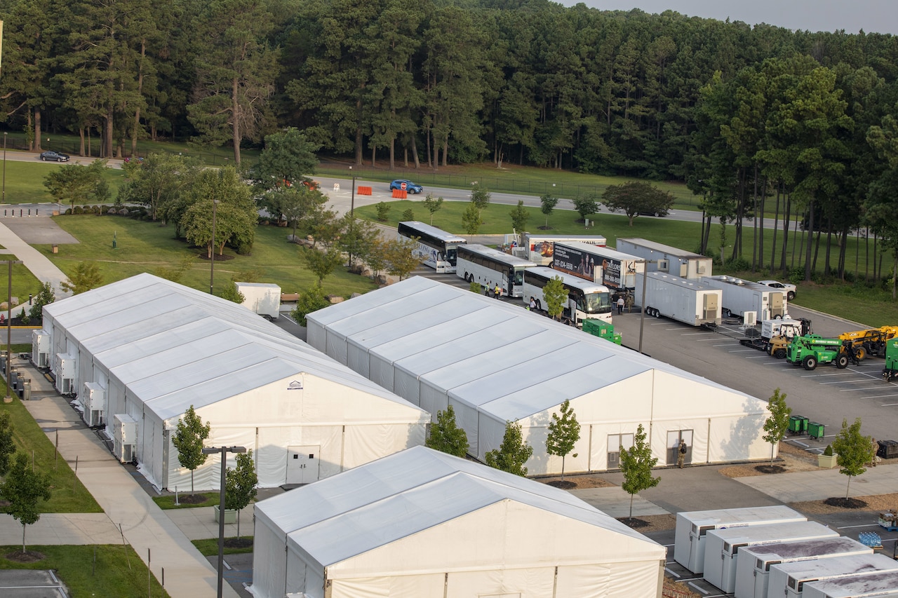 Several buses line up near large temporary structures.