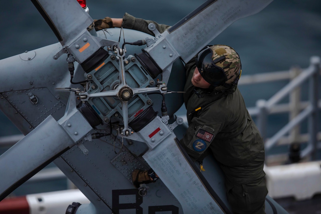 A sailor works on a helicopter's rotor blade.