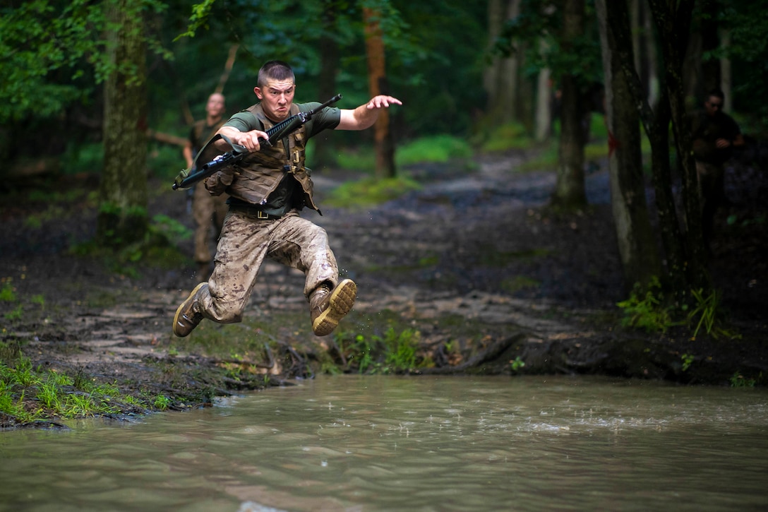 A Marine Jumps over water while holding a weapon.