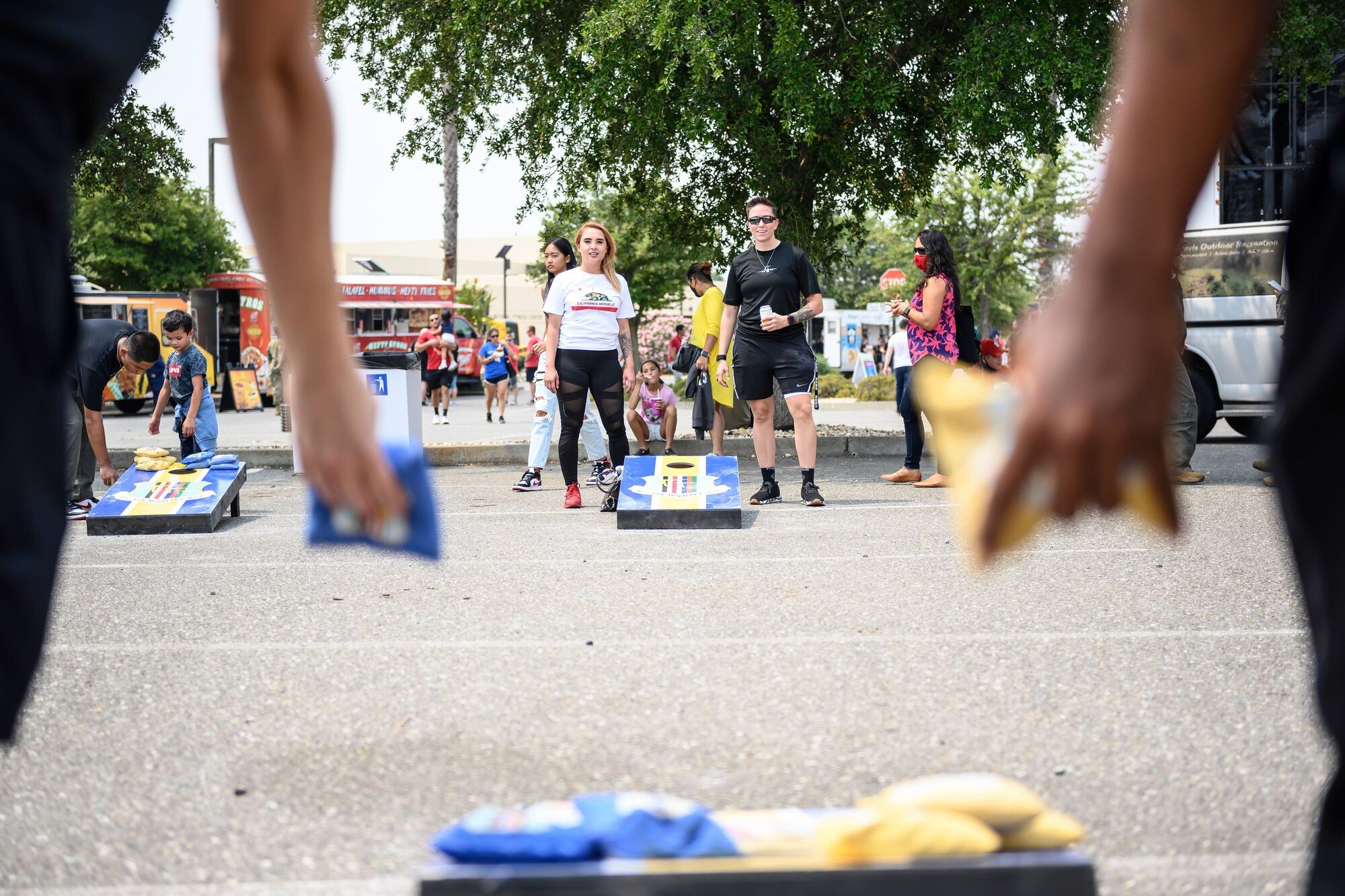 People play cornhole amidst a crowd of people on a sunny day