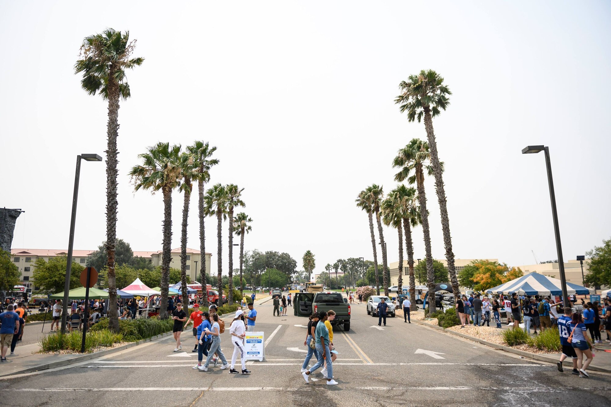 People cross a street while festivities go on on either side of it on a sunny day