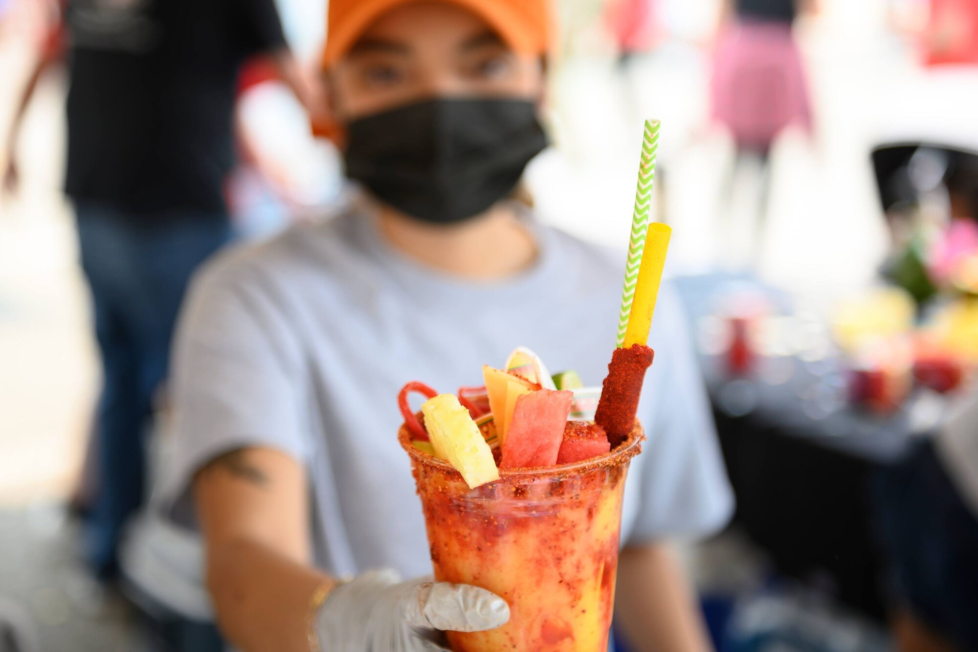 A woman wearing a hat extends out a tropical fruit drink on a sunny day