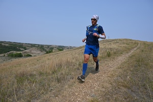 Senior Master Sgt. Brandon Miller runs down a dirt path in the rugged badlands of North Dakota during the Maah Daah Hey Trail 107.3-mile ultramarathon held July 31 through Aug. 1, 2021.