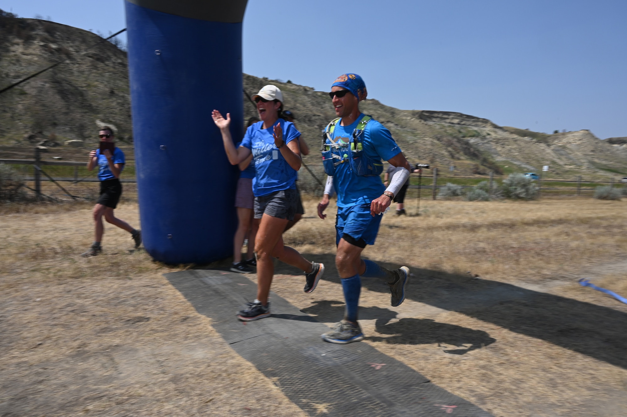 Senior Master Sgt. Brandon Miller runs across the finish line beside his fiance at the Maah Daah Hey Trail 107.3-mile ultramarathon, Medora, N.D., Aug. 1, 2021