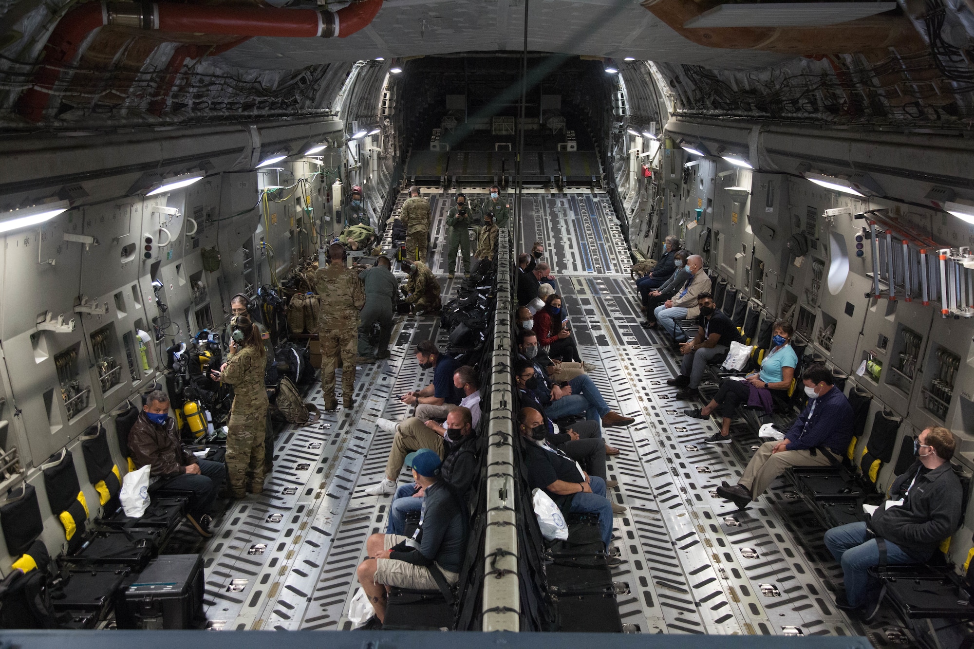 Civilian employers sit in the cargo bay of a military aircraft.