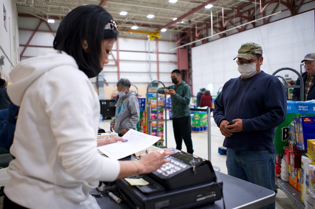 JOINT BASE ELMENDORF-RICHARDSON, Alaska -- Cheryl Bault, Anchorage Area Commissary store associate, rings up groceries for retired Alaska Army National Guard Sgt. 1st Class Harry Alexi during a Commissary sale Aug. 7, 2021, at the Alaska Army National Guard Aviation Facility, Bethel, Alaska. An Alaska Air National Guard C-17 Globemaster III moved tons of groceries and supplies from Joint Base Elmendorf-Richardson to Bethel to offer the goods to eligible residents at discount prices. (U.S. Air National Guard photo by David Bedard/Released)