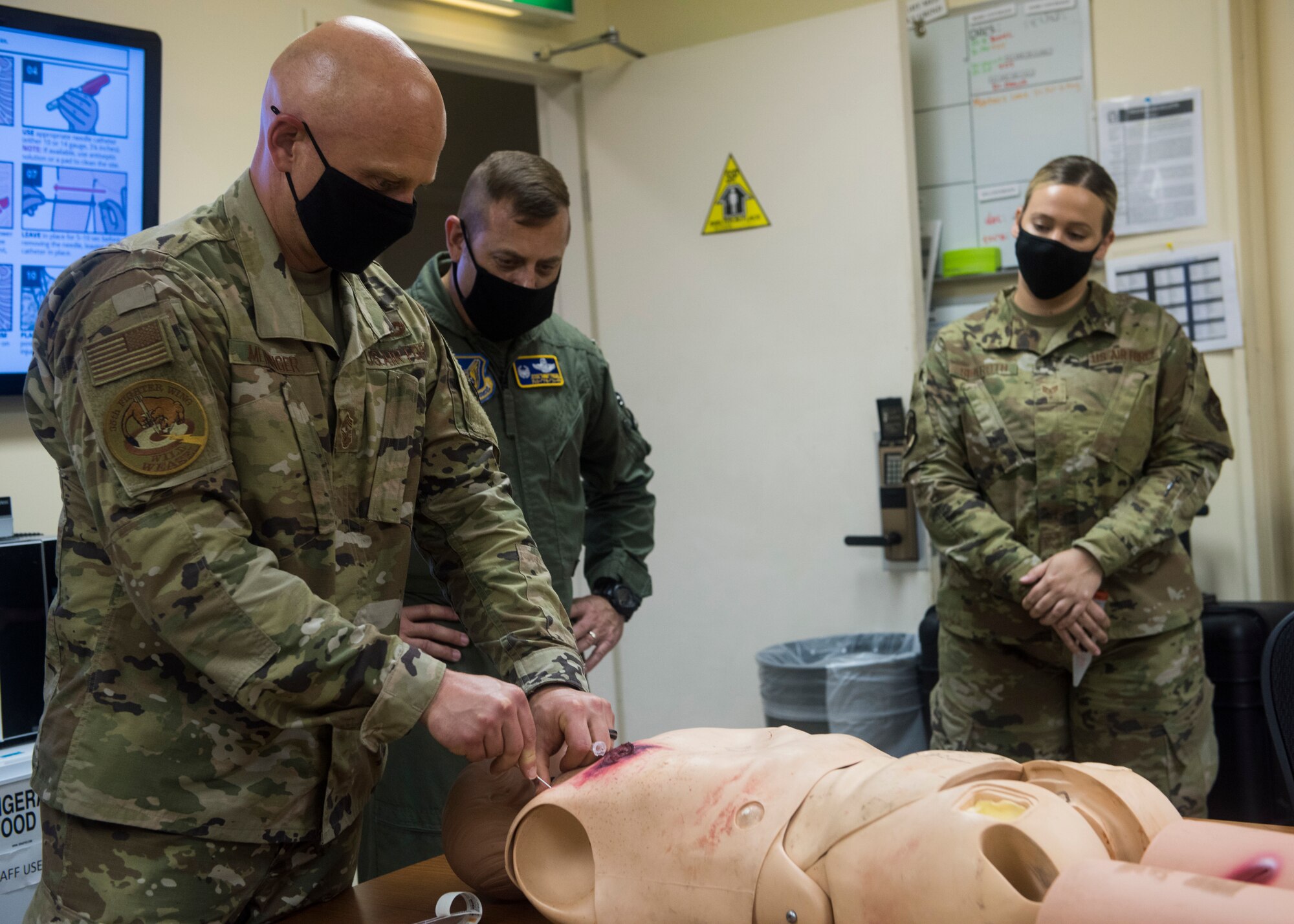 Servicemembers in uniform use a needle on a simulated patient.