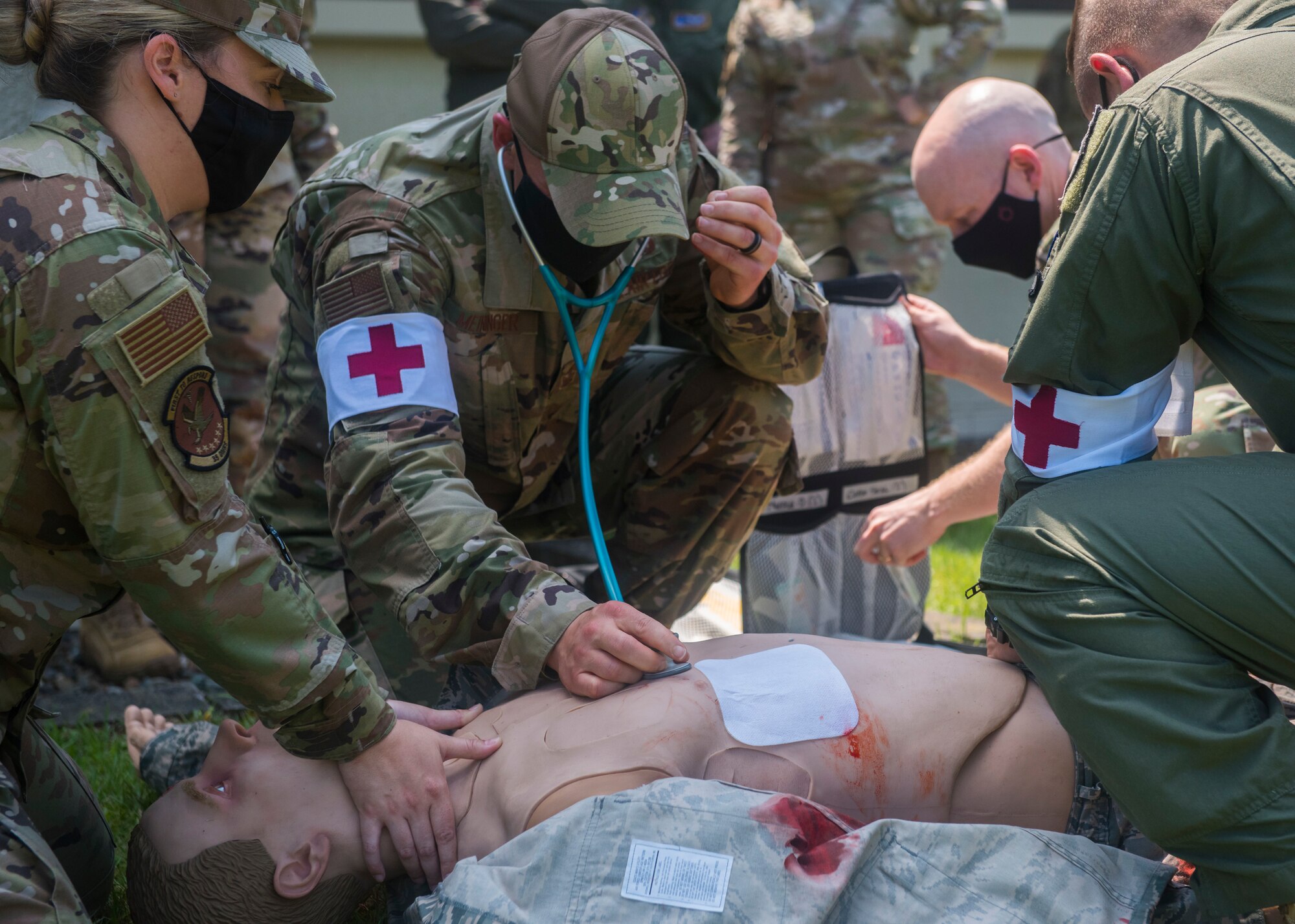 Group of servicemembers in uniform check for vitals on a simulated wounded patient