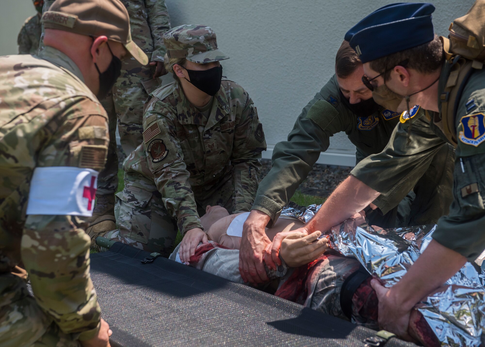 Servicemembers in uniform prepare to lift a simulated patient onto a stretcher.