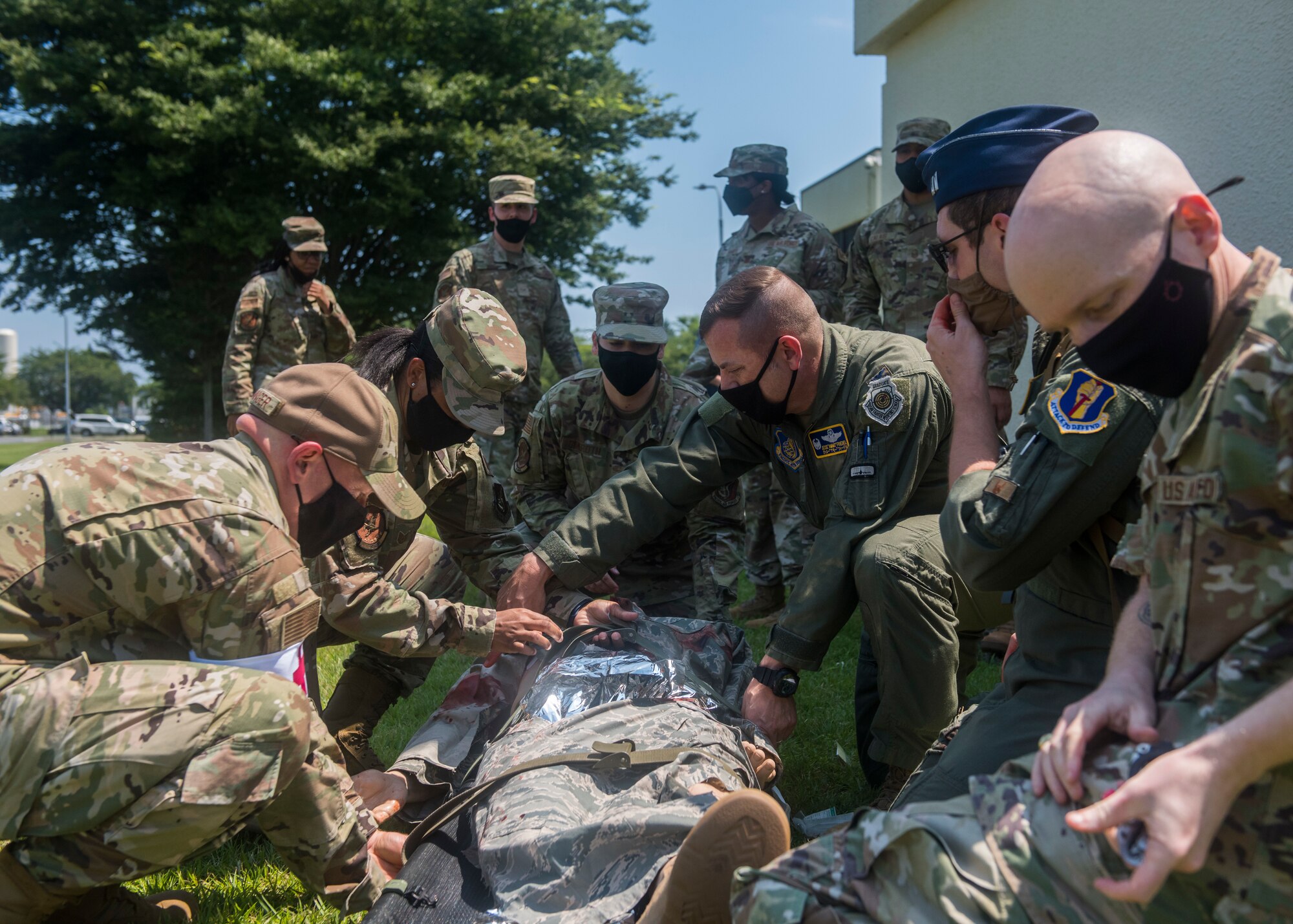 Group of servicemembers in uniform apply medical aid to simulated patient.