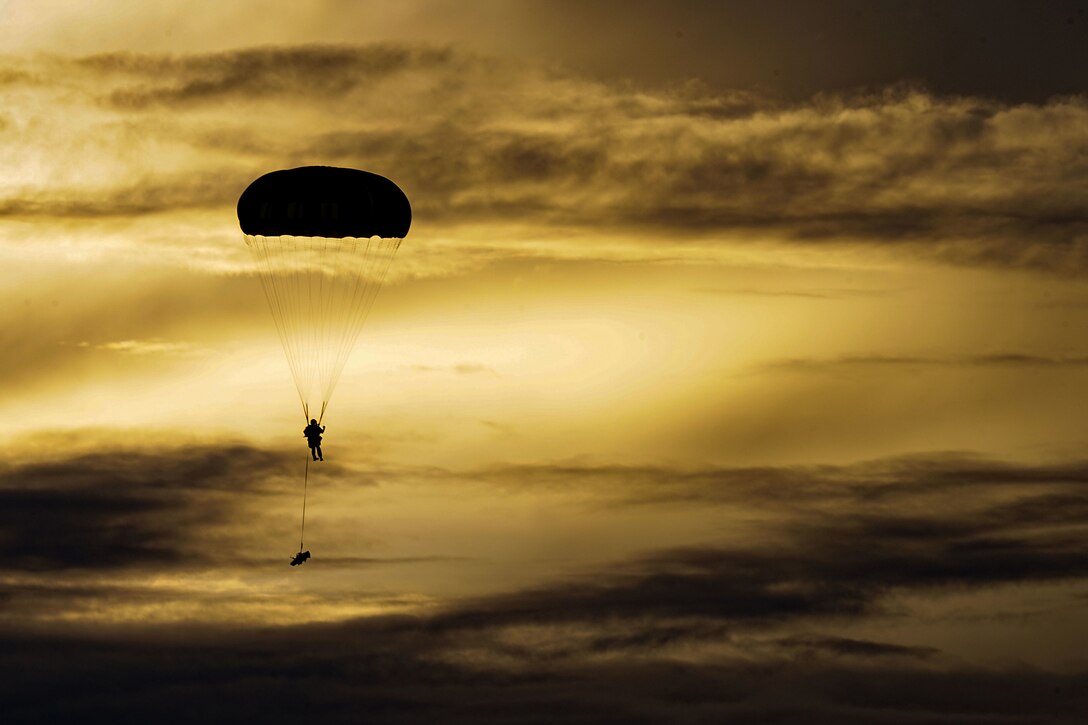 A parachutist descends to the ground against a golden sky.
