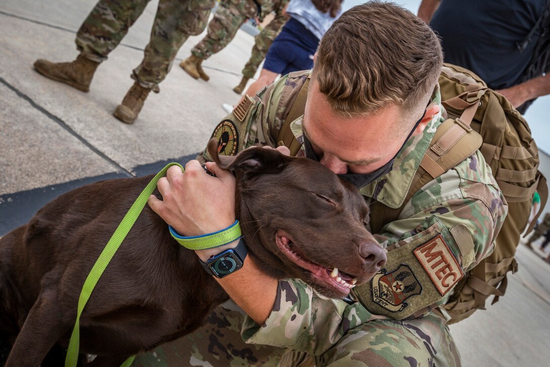 An airman hugs a dog who appears to be smiling.