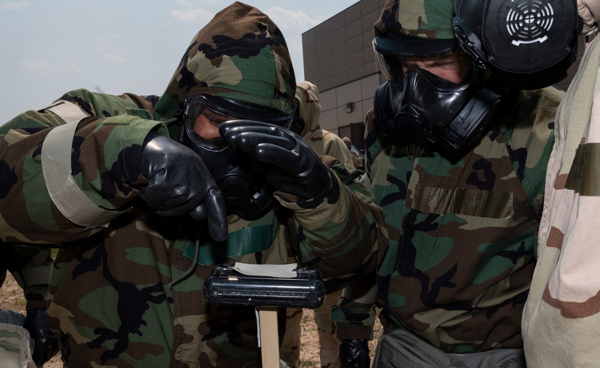 People dressed in chemical gear examine a piece of paper outside.