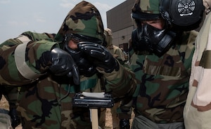People dressed in chemical gear examine a piece of paper outside.