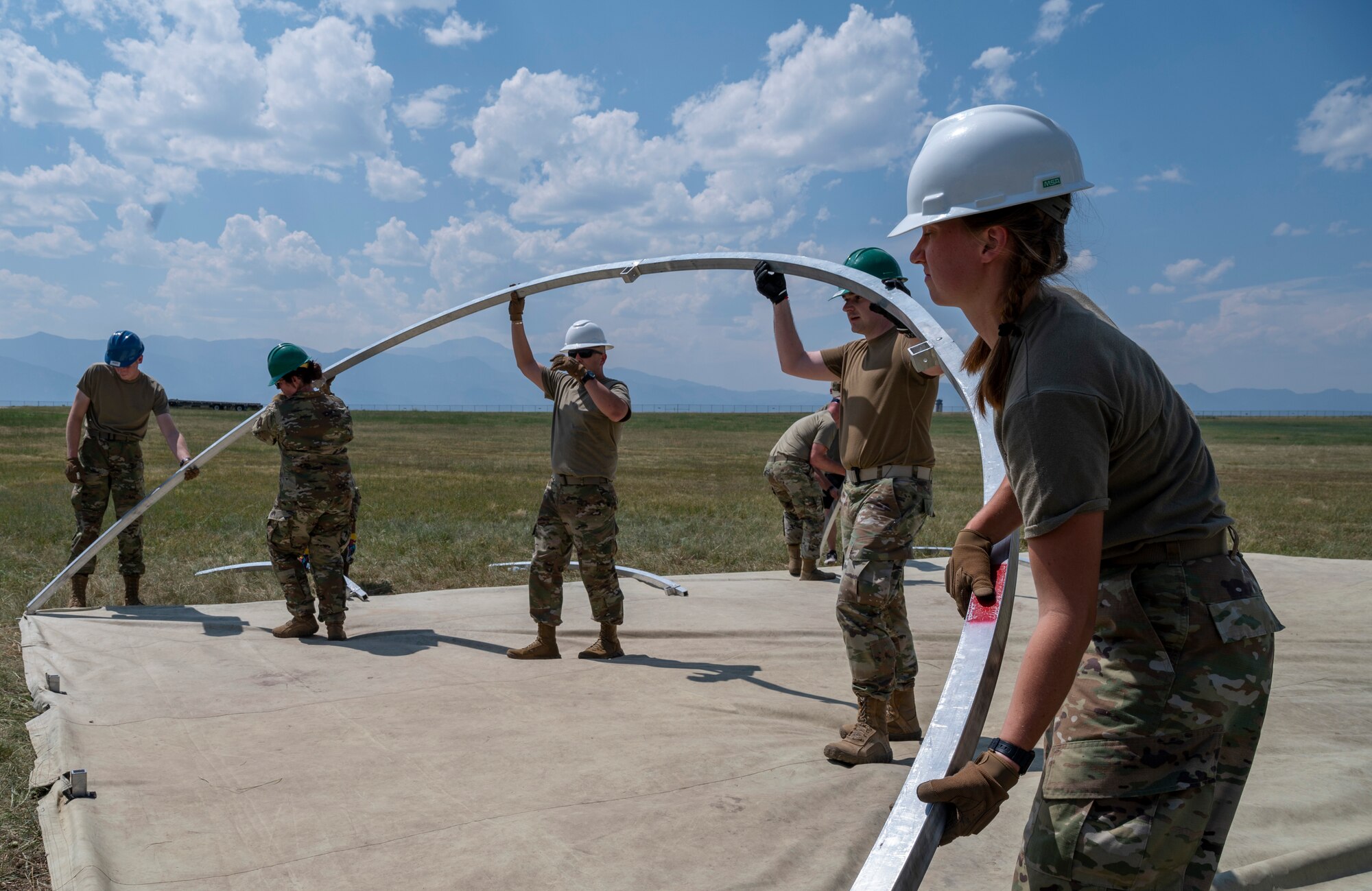 People in hardhats standing outside assemble a metal structure.