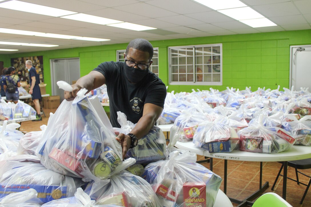 A man places a large bag of food on top of a pile of other bags of food.