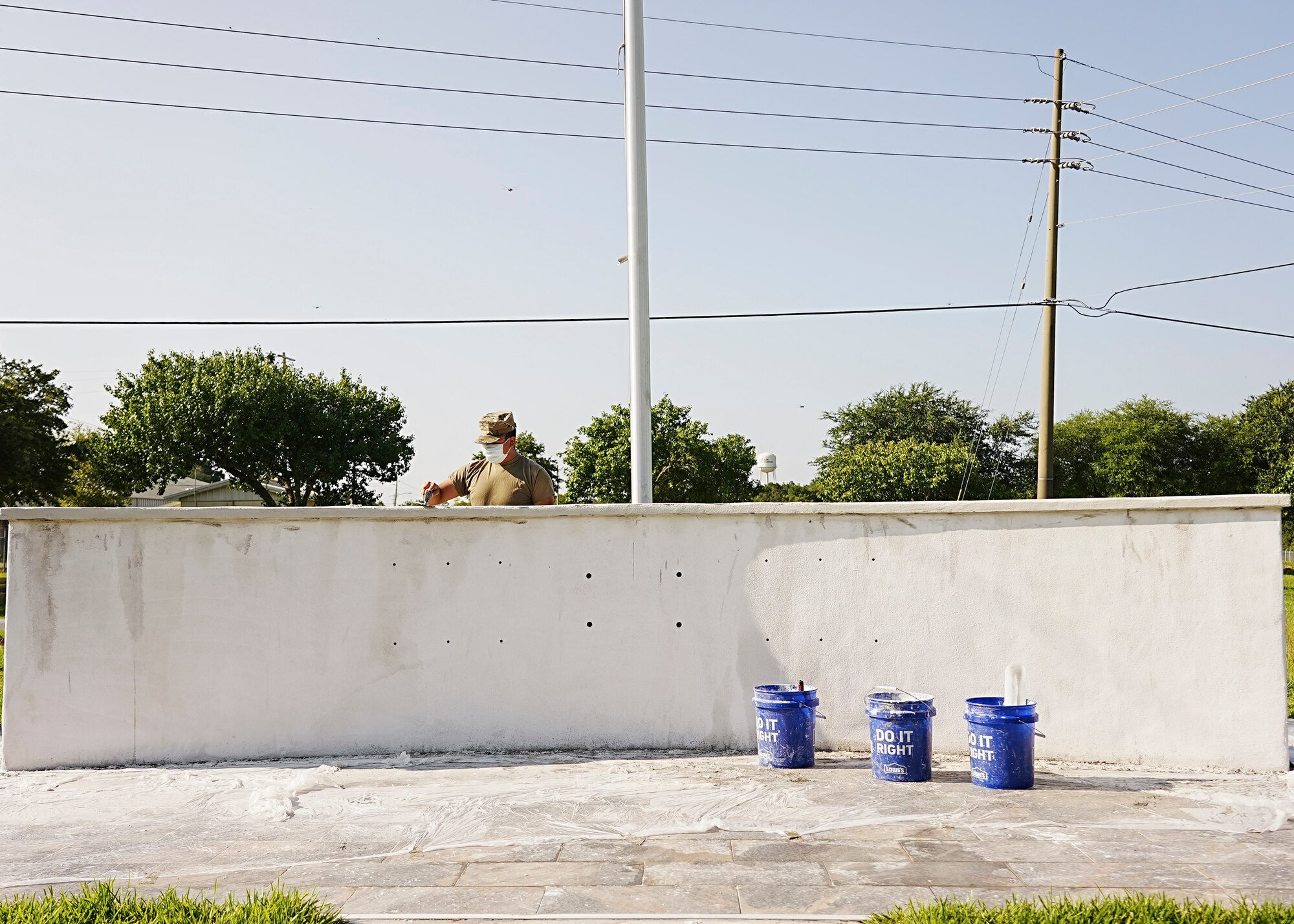 Airman behind concrete wall smooths stucco over surface.