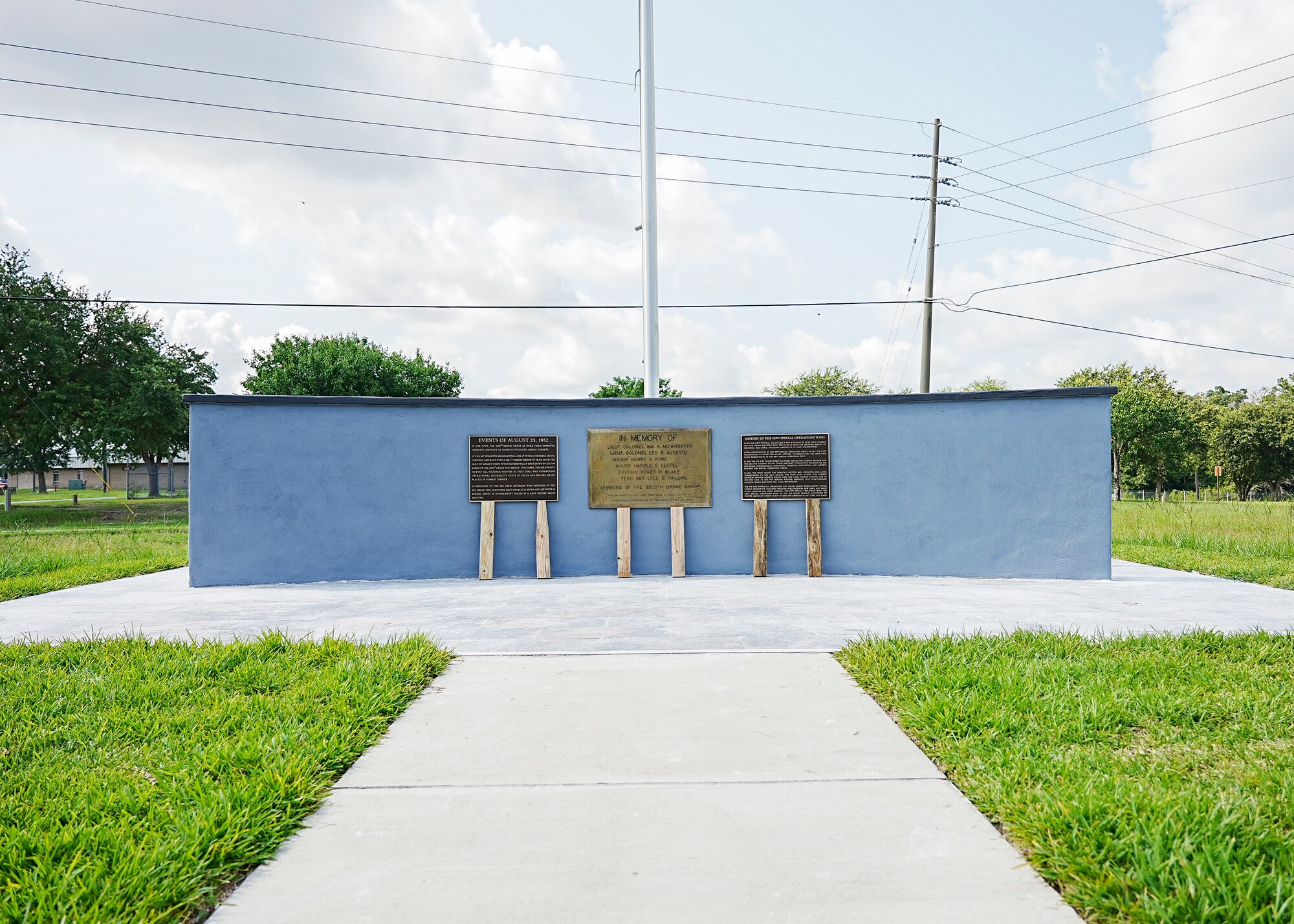 Concrete wall with plaques and flagpole with sidewalk leading to tile plaza around monument.