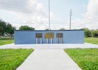 Concrete wall with plaques and flagpole with sidewalk leading to tile plaza around monument.