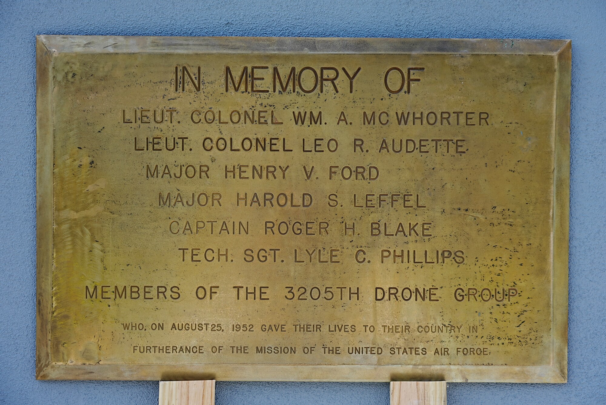 Gold plaque sits on two planks while leaning on concrete wall.