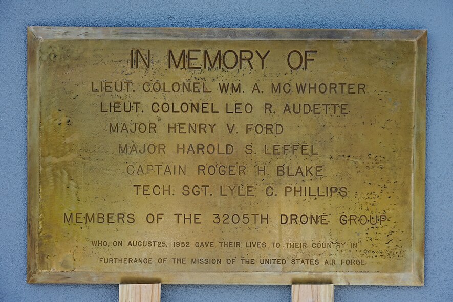 Gold plaque sits on two planks while leaning on concrete wall.