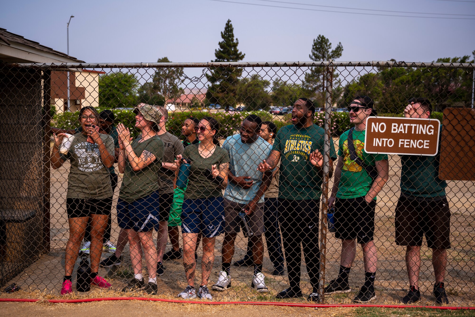 A group of young people hang out next to a fence on a softball field.