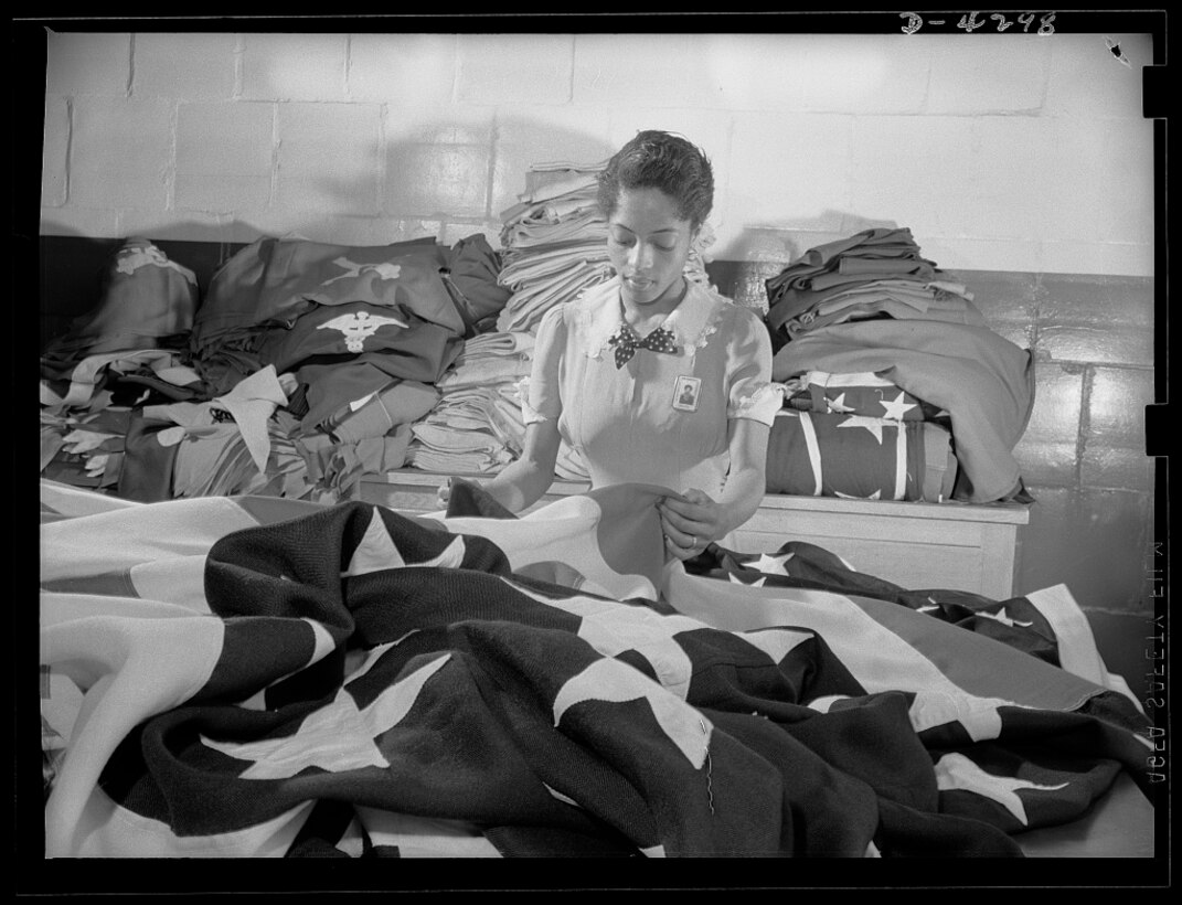 A young woman worker assists in the creation of American flags for military activities at the Philadelphia Quartermaster Depot. DLA Troop Support has been involved in the art of flag making since the early 1800s when Betsy Ross made more than 50 garrison flags for the Schuylkill Arsenal. Today, Troop Support's Clothing and Textiles flag room creates patriotic flags for all branches of the armed services and is the sole producer of the hand-embroidered presidential and vice presidential flags