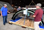 Photo shows three men looking closely at a large aircraft part