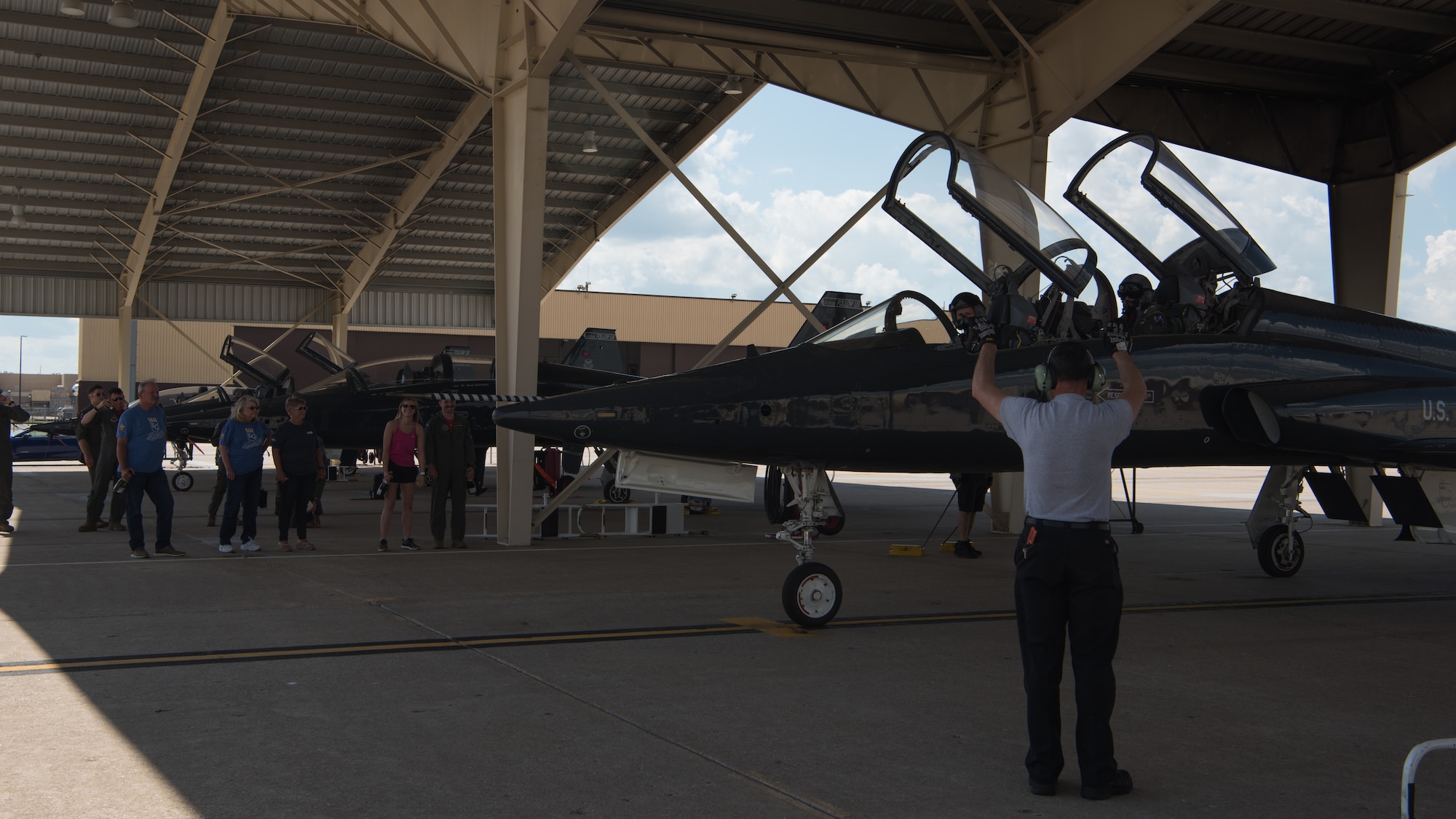 A crew chief marshals a T-38 Talon into its parking spot under the sun shades.