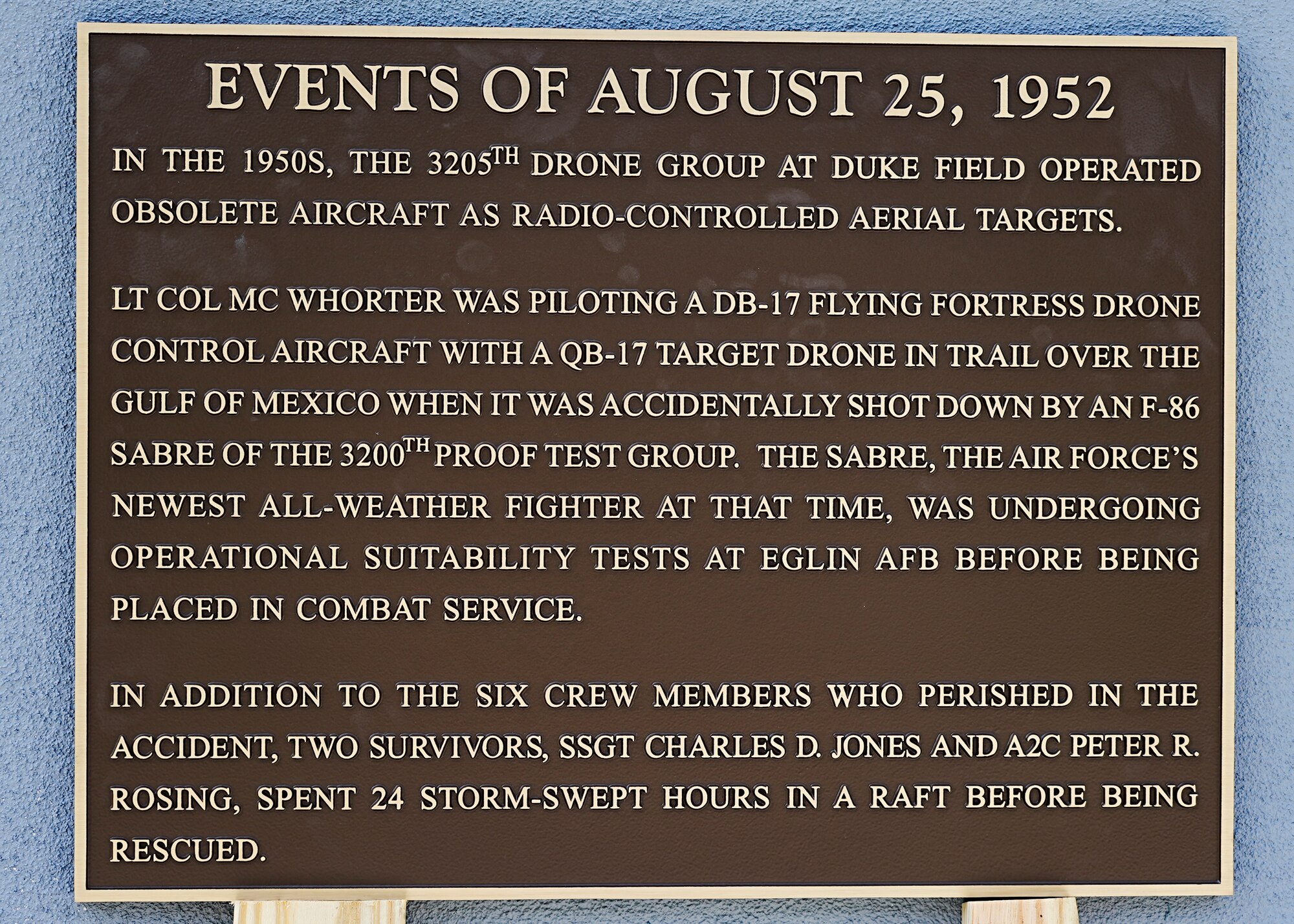 Metal plaque sits on two wood planks while leaned against concrete wall.