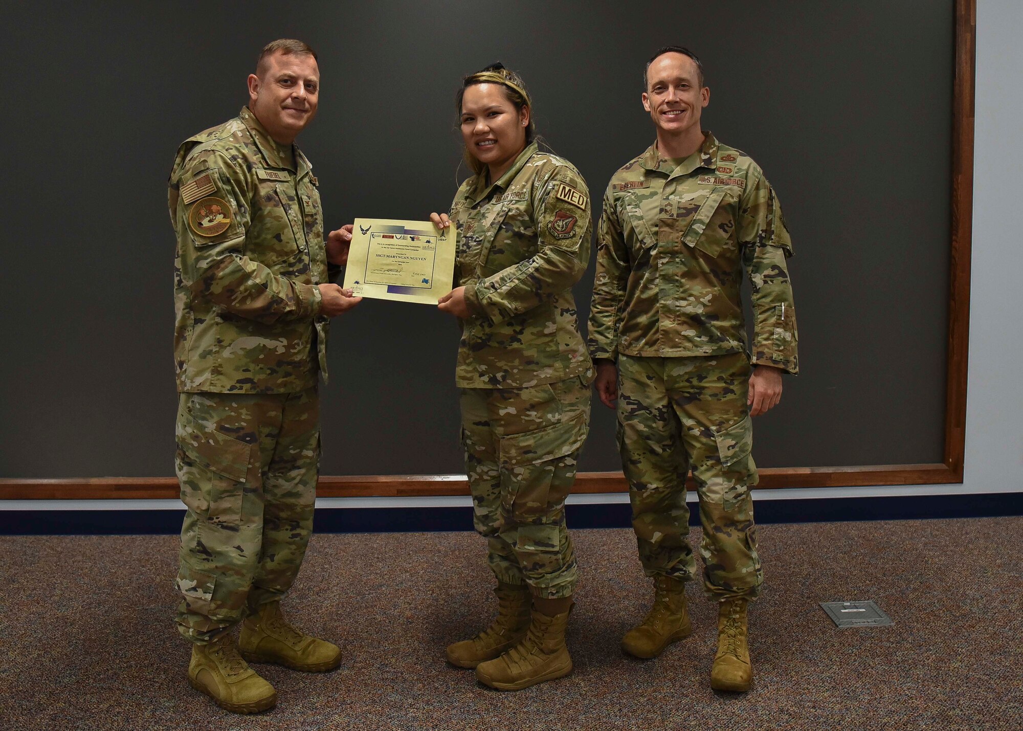 Three military members pose for a picture while the left one awards the center member.