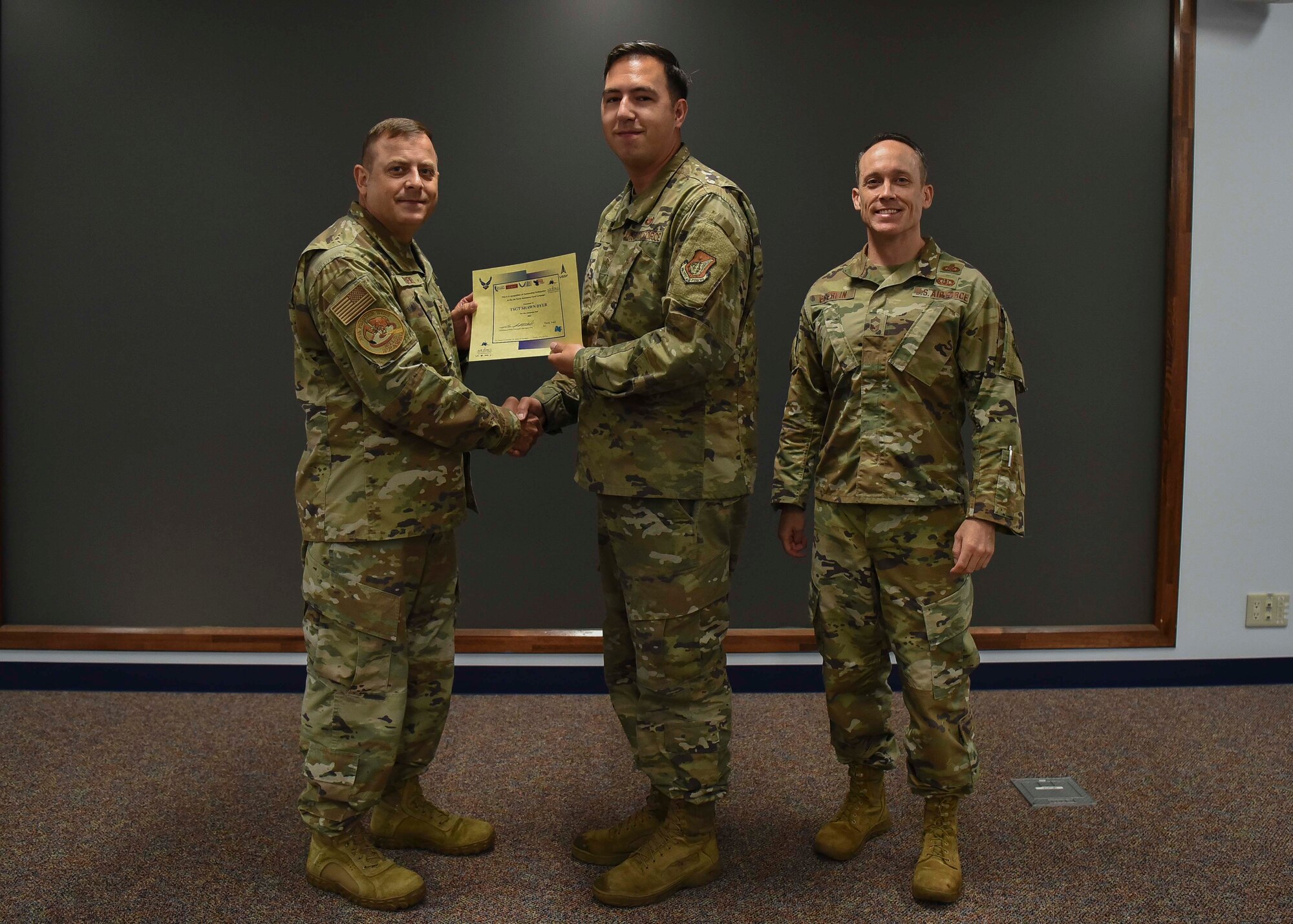 Three military members pose for a picture while the left one awards the center member.