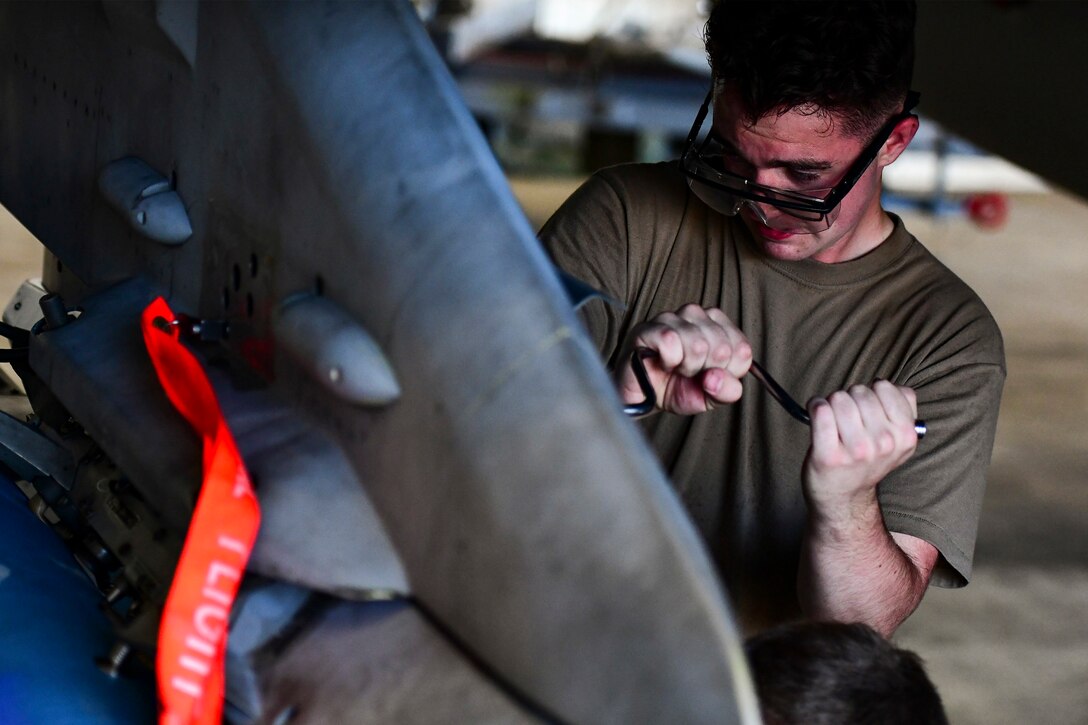 An Airman secures a bomb onto a jet.