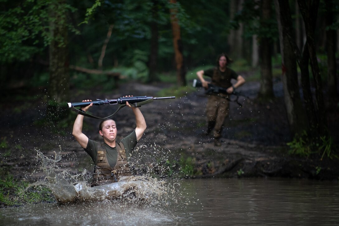 A Marine jumps into water holding a rifle above her head.