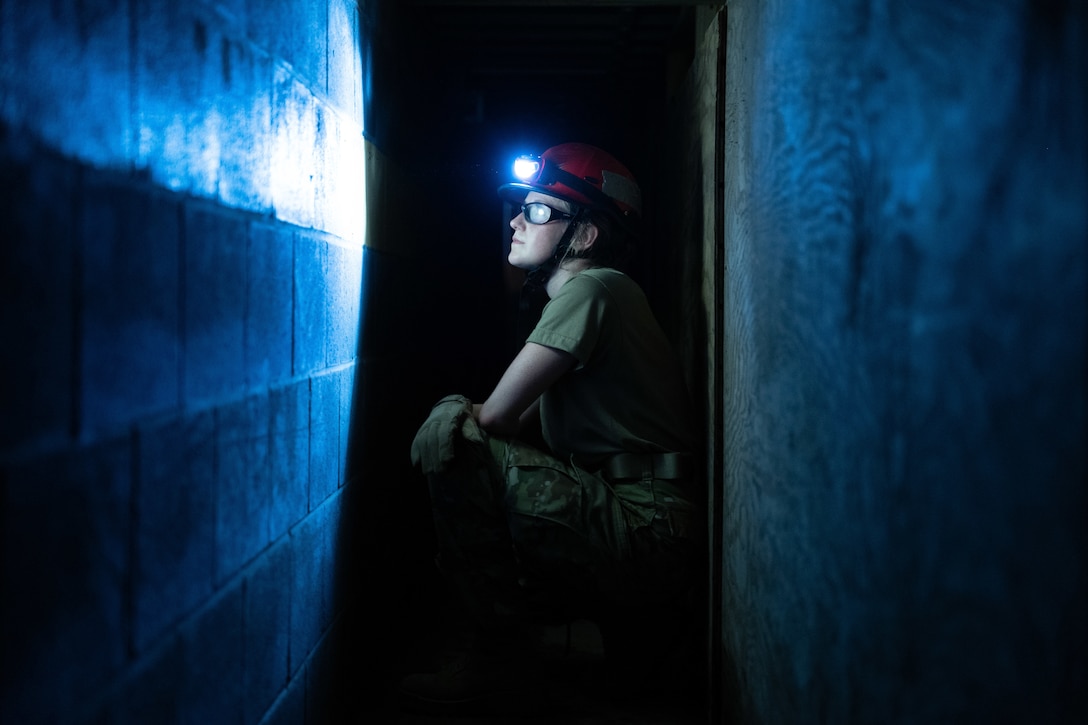 An airman uses a headlamp to see in a dark tunnel.