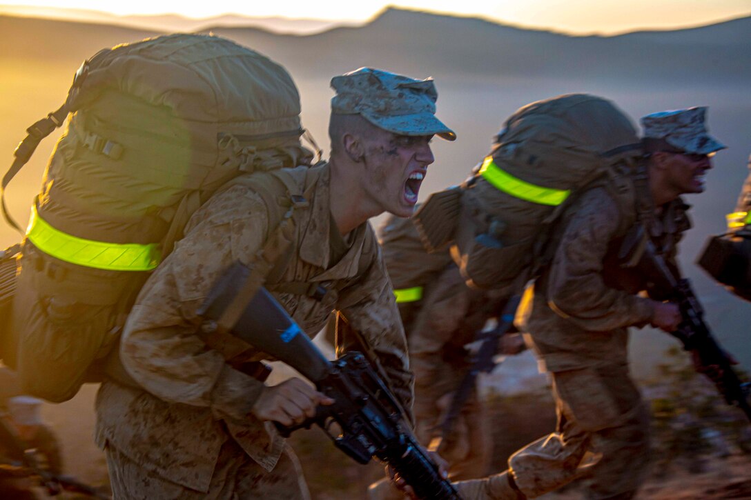Two Marine Corps recruits run side by side while carrying weapons.