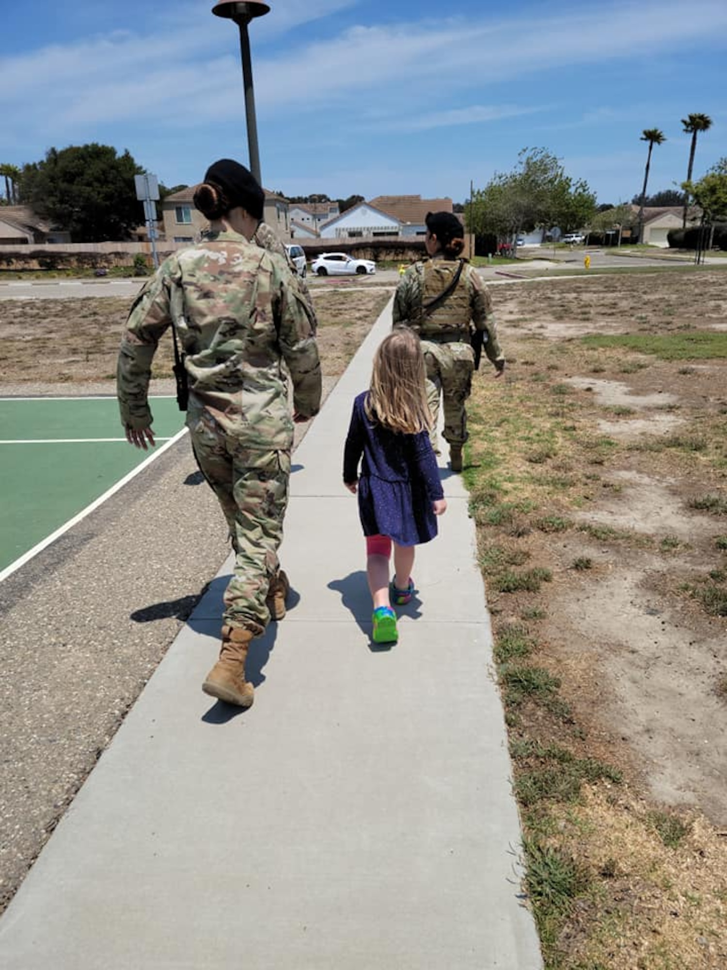 Two police officers walk down sidewalk with little girl