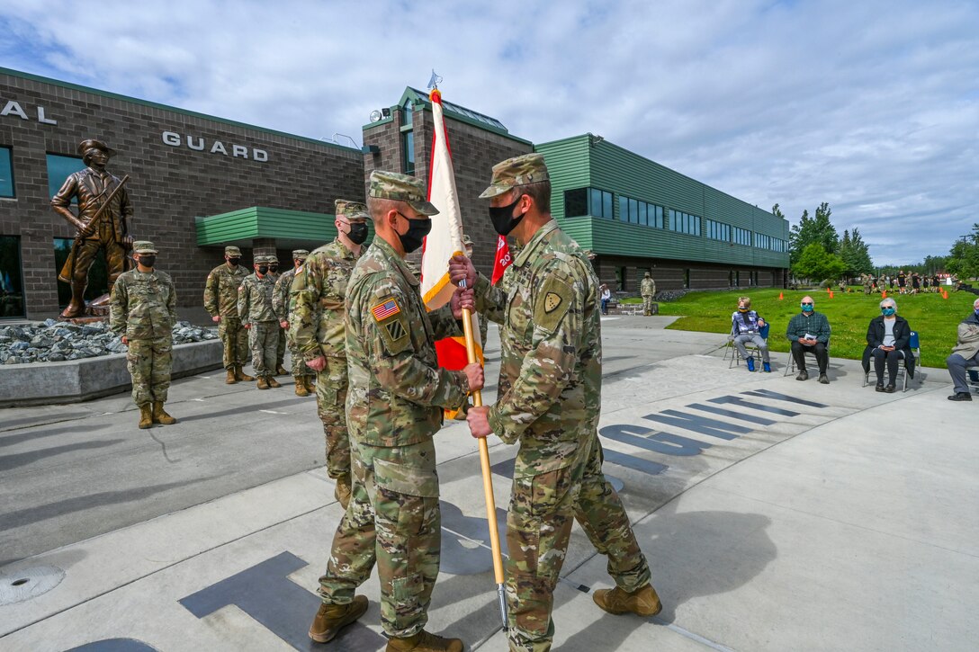 Brig. Gen. Charles “Lee” Knowles, commander of the Alaska Army National Guard, passes the unit guidon to Col. Thomas “Alex” Elmore, incoming commander of the 297th Regional Support Group, during a ceremony at the Lestenkof Plaza on Joint Base Elmendorf-Richardson, Alaska, August 7, 2021. The passing of the unit colors symbolizes the transfer of responsibility from the outgoing to the incoming commander. (U.S. Army photo by Sgt. Heidi Kroll)