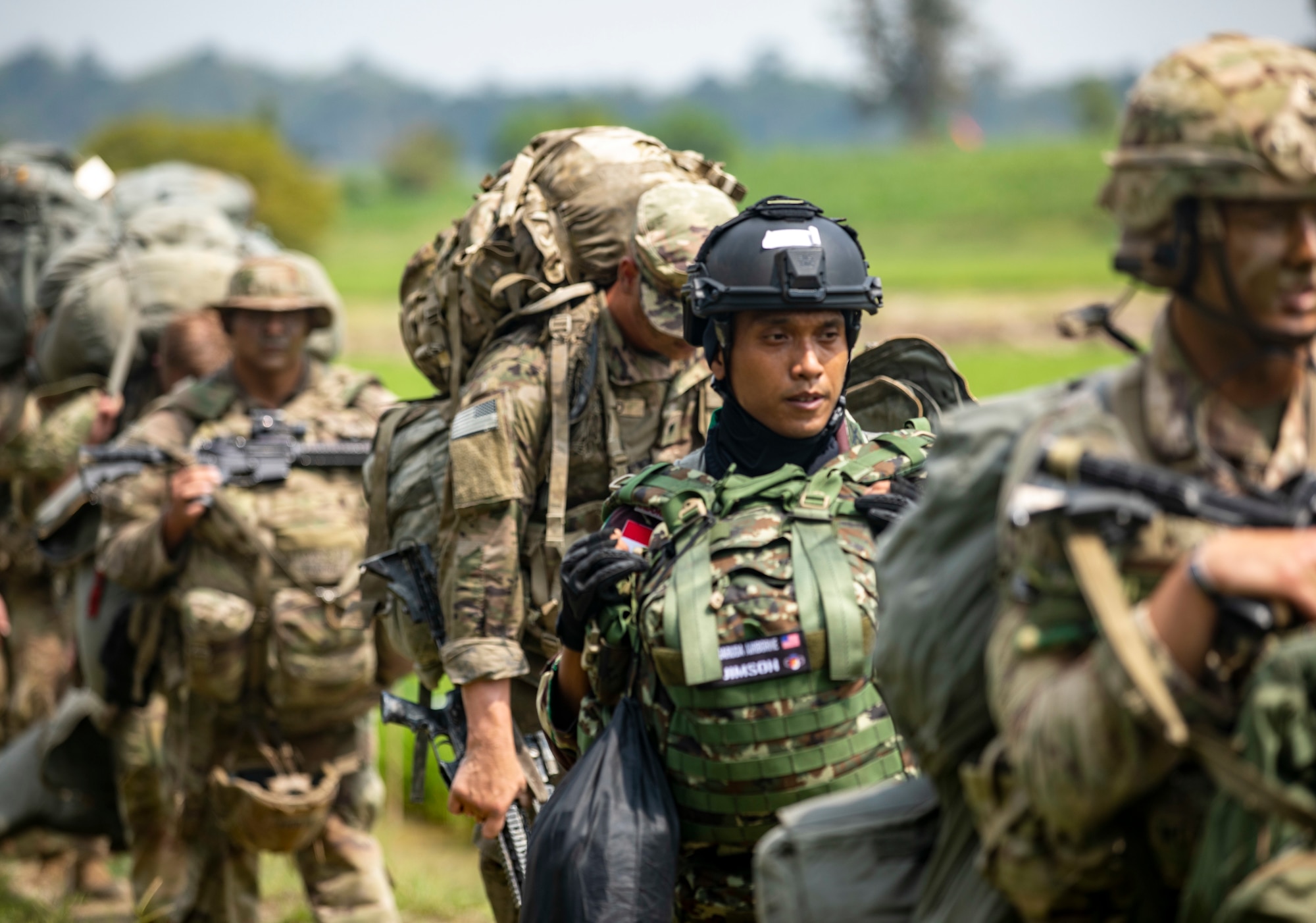 Soldiers walk through a field with their gear.