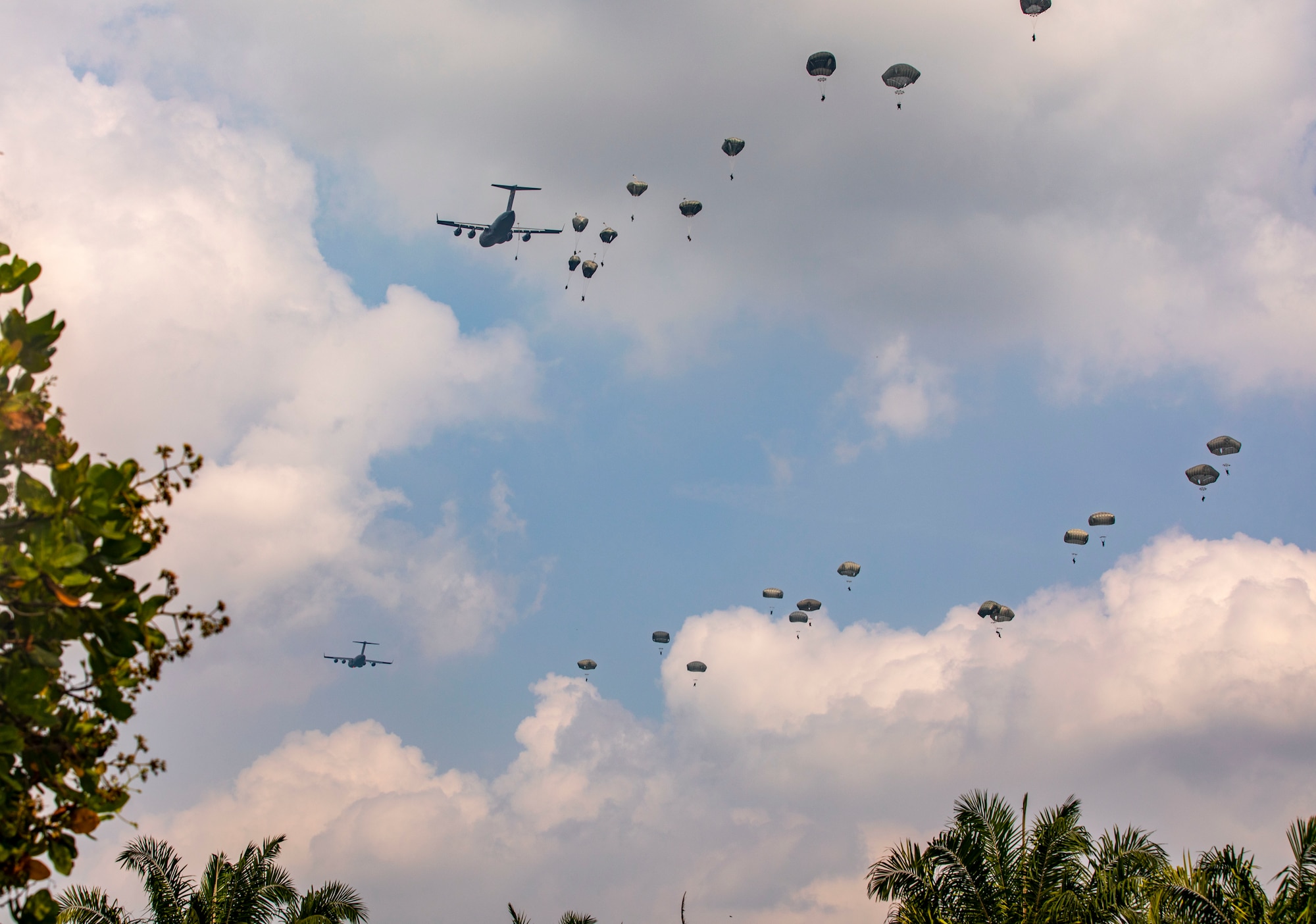 A plane flying by while dropping paratroopers.
