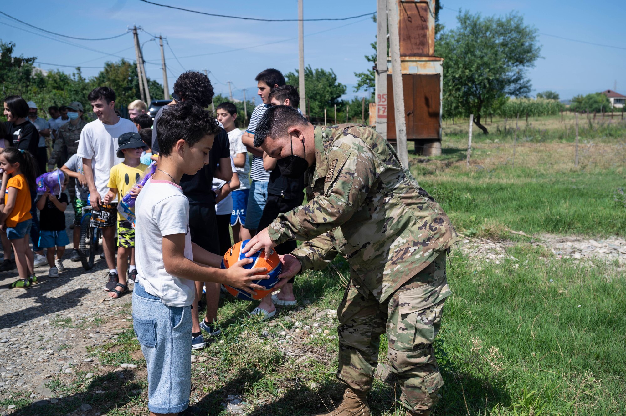 U.S. Air Force Staff Sgt. Tyler Nakamura, 291st Combat Communication Squadron cyber transport, pumps up a ball for a child at a toy giveaway during exercise Agile Spirit 21
