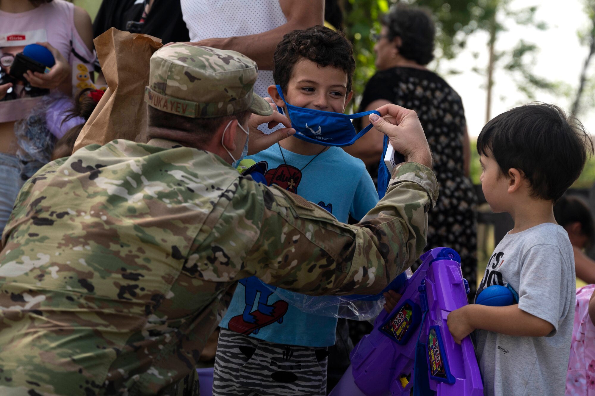 U.S. Air Force 2nd Lt. Dennis Tyukayev, 86th Operations Support Squadron operations officer, places a U.S. Air Force cloth face covering over the face of a child during a toy giveaway during exercise Agile Spirit 21