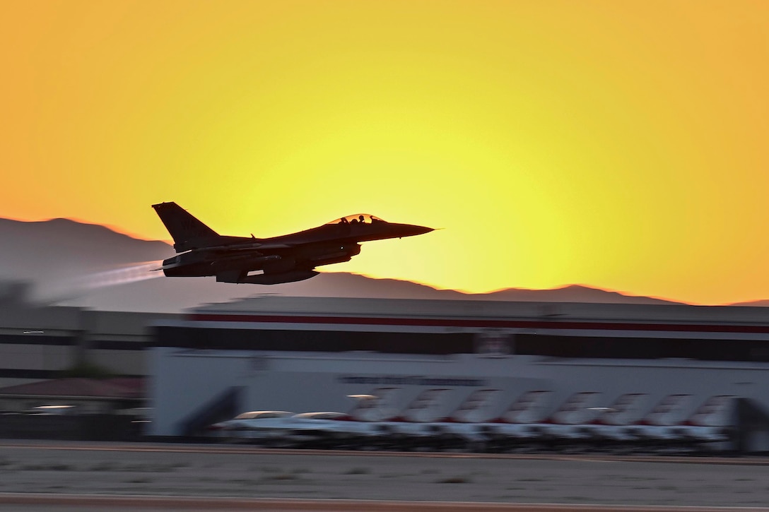 A fighter jet takes off at twilight with a golden sky.