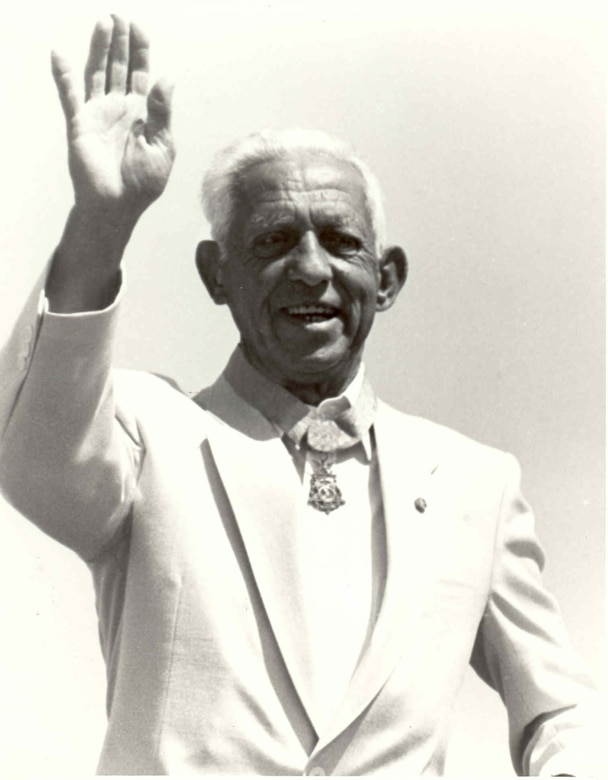 A man wearing a medal around his neck waves.