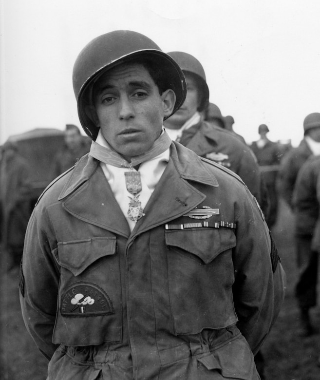 A young soldier in fatigues and a helmet wears a medal around his neck.