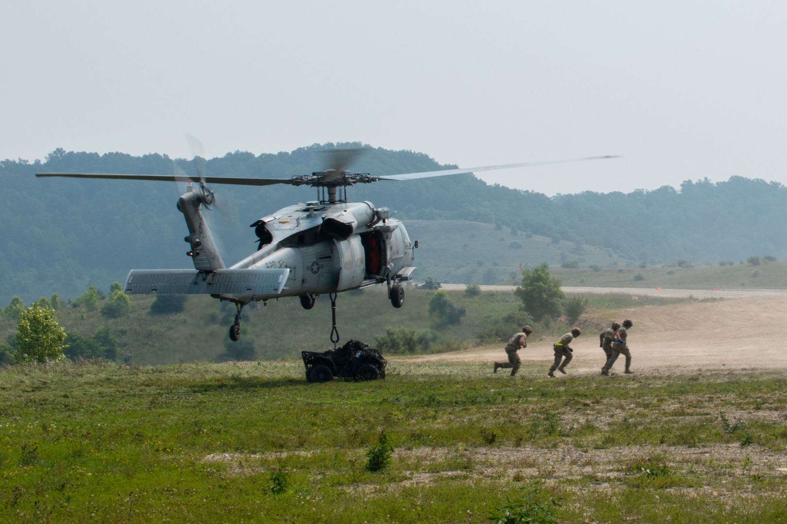 Airmen from the 123rd Airlift Wing, Kentucky Air National Guard, and a Navy MH-60 Seahawk from Helicopter Sea Combat Squadron Nine, Naval Air Station Norfolk, Virginia, offload an all-terrain vehicle during sling load training at Sentry Storm 2021 at Camp Branch, Logan County, West Virginia, July 20, 2021.