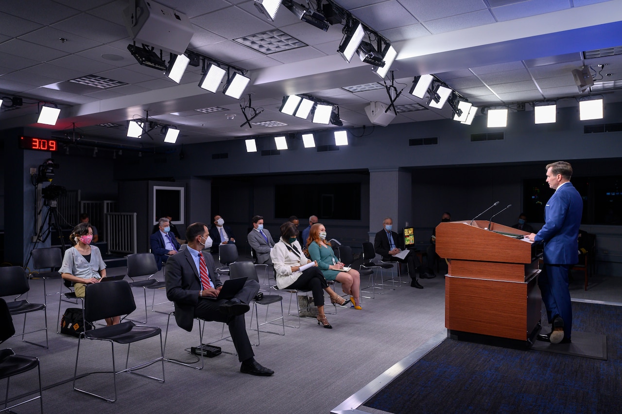 A man speaks to a roomful of reporters.