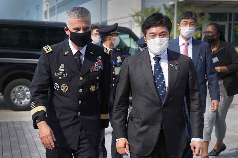 A U.S. Army general walks next to a Japanese government leader, both men wearing face masks.