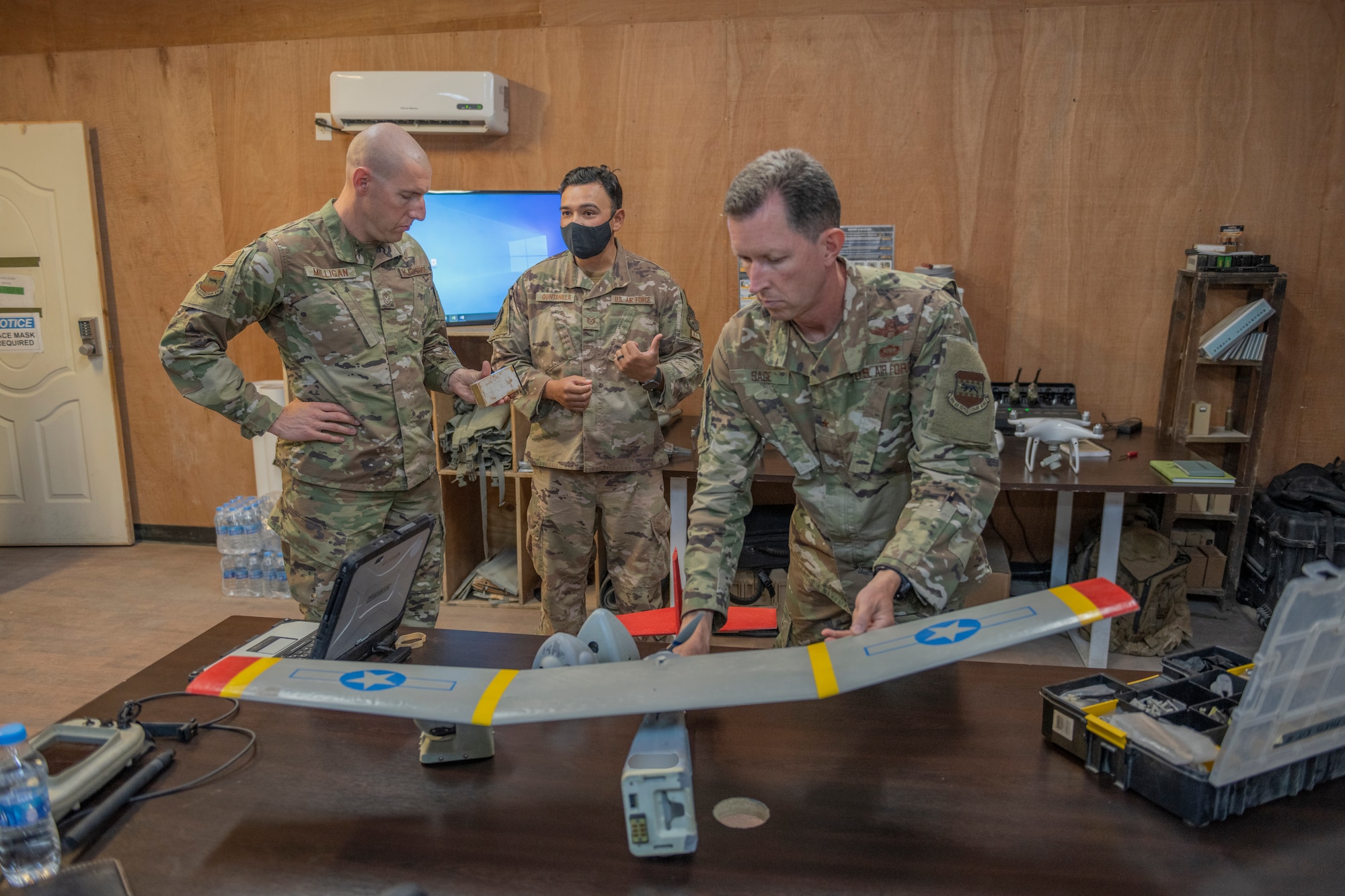 U.S. Air Force Tech. Sgt. Jerry Quintanilla, center, 332nd Expeditionary Security Forces Squadron noncommissioned officer of raven B, explains to Brig. Gen. Christopher Sage, right, 332nd Air Expeditionary Wing commander, and Chief Master Sgt. Sean Milligan, 332nd AEW command chief, how drones are utilized July 22, 2021, in an undisclosed location somewhere in Southwest Asia. The immersions provide 332nd AEW leadership an opportunity to interact with Airmen and receive a detailed view of unit capabilities. (U.S. Air Force photo by Senior Airman Cameron Otte)(This image is blurred for security reasons)