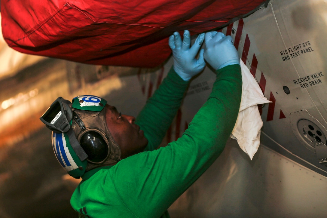 A sailor uses a rag to apply a compound to an aircraft.